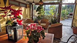 A cozy indoor seating area with wicker furniture, potted plants, and a view of the garden through a glass door.