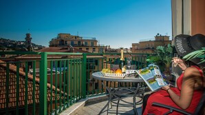 A balcony with a table set for two, featuring a bottle of champagne, a glass, and a basket of fruit.