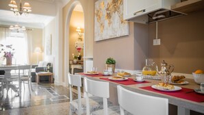 A modern kitchen with a marble countertop, white chairs, and a dining table set for breakfast.