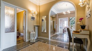 A hallway with a polished stone floor, a mirror, a chandelier, and a reception desk with a potted plant.