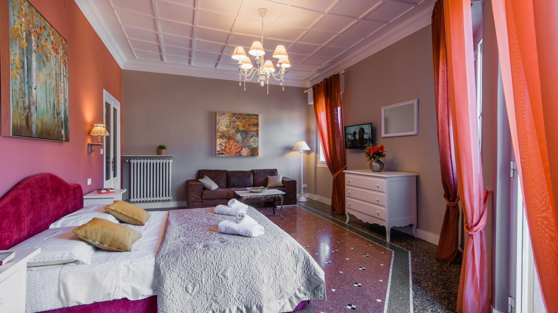 Ett hotellrum med en säng, en soffa, en byrå, ett element och en tavla på väggen.