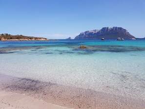 A beach with clear turquoise water, a rocky outcrop, and boats in the distance. - Villa with parking and veranda, 900 m from the beach - San Teodoro (San Teodoro)