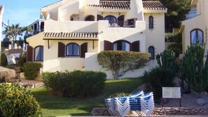 Een gebouw in mediterrane stijl met een zwembad, omringd door groen en cactussen.