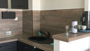 A compact kitchen with dark cabinets, a sink, and a countertop. A 'CUSINE' sign is visible on the wall. - Hyper city center with sea-view terrace, right on the beach. (Bandol)