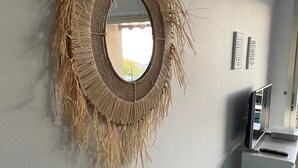 A circular woven mirror on a wall, a small white shelf with a remote control, and a blue desk with a printer and a roll of paper. - Hyper city center with sea-view terrace, right on the beach. (Bandol)