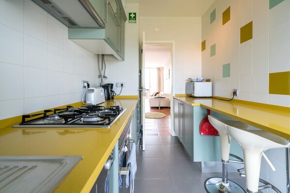 A modern kitchen with a yellow countertop, stainless steel appliances, and a view into a living area. - Contemporary Apartment in heart of Marina, New Decor (Lagos)