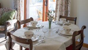 Ein Esszimmer mit einem Tisch für vier Personen, Holzsesseln mit roten Kissen, einer Vase mit Blumen und Blick durch eine Glastür nach draußen.