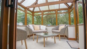 Ein Wintergarten mit Korbmöbeln, einem Glastisch und Blick ins Grüne.
