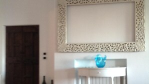 A room with a tiled floor, a white table with a blue vase, a decorative mirror, and two bottles on the floor. - LE QUERCE - Villa with spectacular sea view and swimming pool (Maratea)