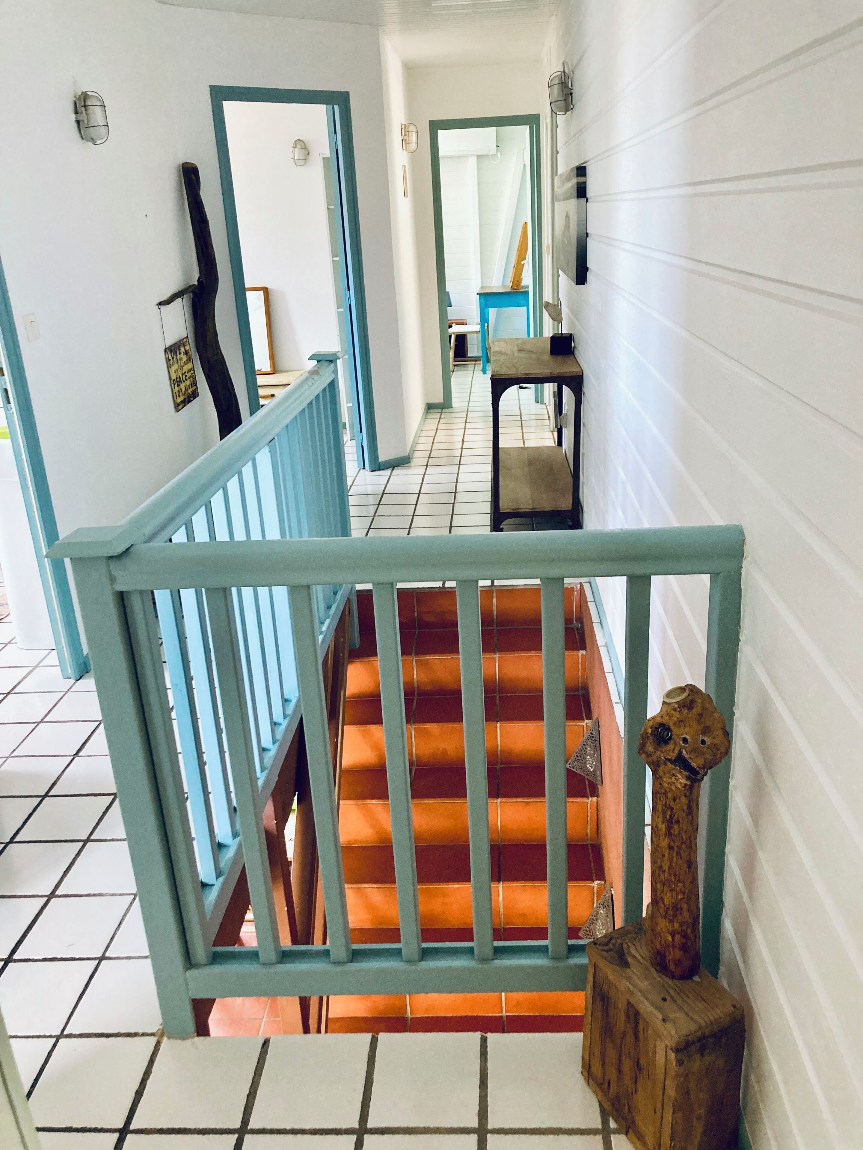 Eine Treppe mit blauen Geländern und orangefarbenen Stufen, die zu einem Raum mit einem Holztisch und einem Stuhl führt.