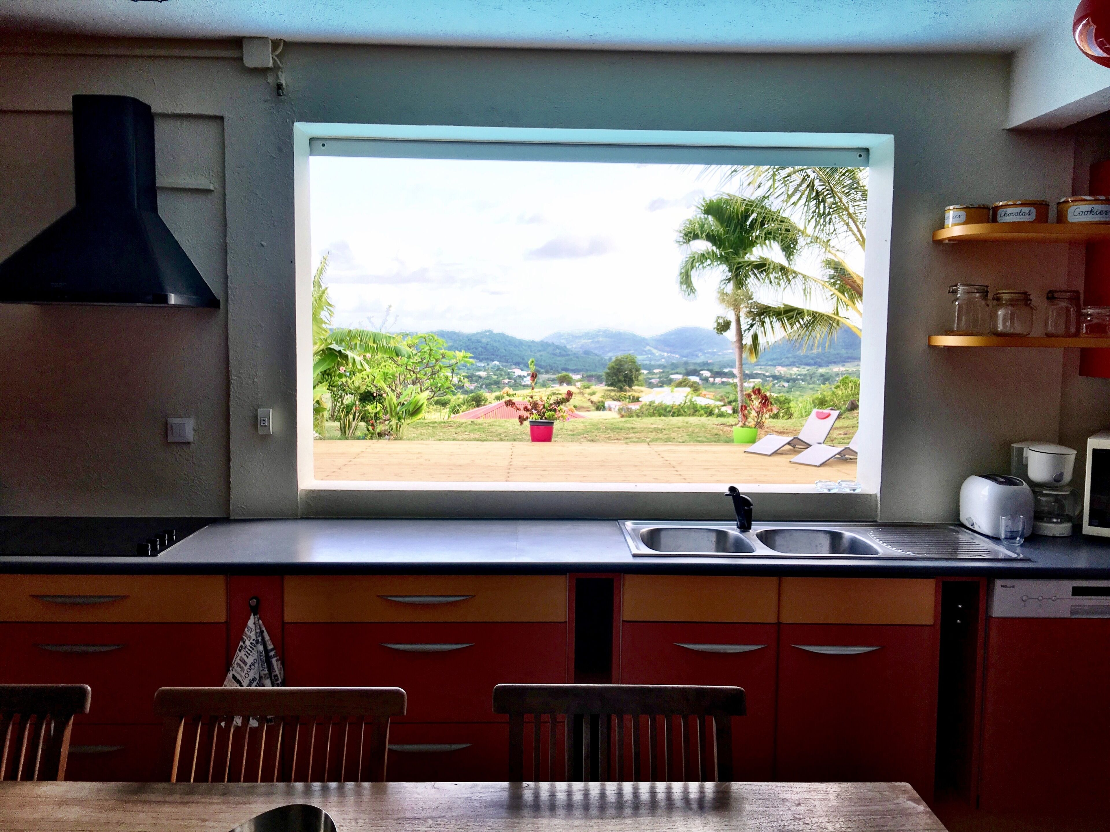 Una cocina con ventana que da a un jardín y montañas.