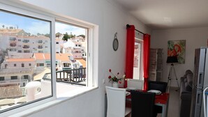 A compact living space with a balcony, a dining area with a table and chairs, a kitchenette, and a view of the cityscape.