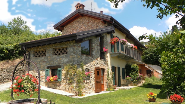 Une maison en pierre dotée d’un balcon, entourée d’une pelouse bien entretenue et de plantes en fleurs.
