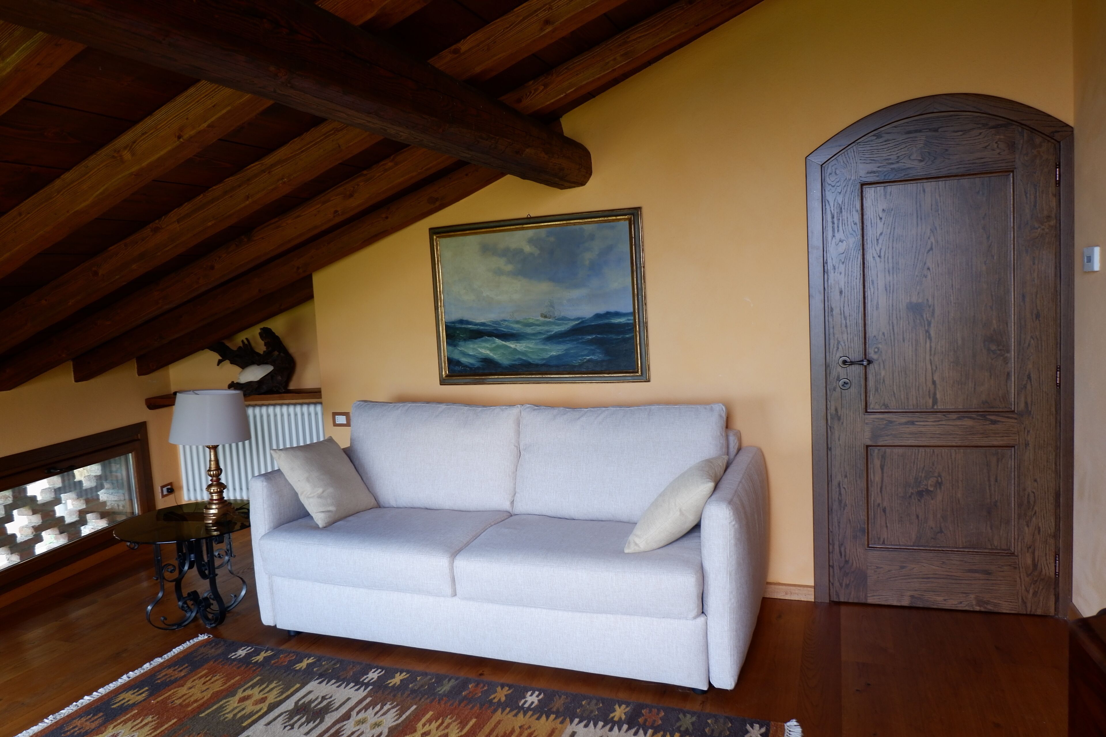 A living room with a light-colored sofa, a wooden door, and a framed painting of a seascape.