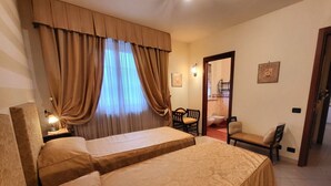 A hotel room with two beds, a sitting area with a chair and a table, a bathroom visible through an open door, and a wall-mounted light fixture. - Close to centre of Lucca. Perfect base for exploring. Exclusive use of pool, A/c (Lucca)