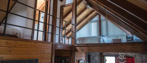A loft-style bedroom with a sloped ceiling, wooden beams, and a large window.