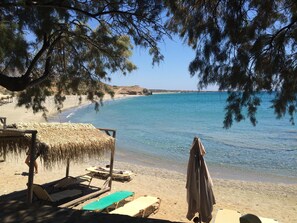 Ein Strand mit Liegestühlen und Sonnenschirmen, klarem blauen Wasser und einem Baum im Vordergrund.