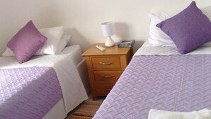 Une chambre d’hôtel avec deux lits, chacun recouvert d’une couvre-lit violette et agrémenté d’oreillers blancs. On y trouve une table de chevet en bois avec une lampe, une boîte de mouchoirs et une télécommande. Un miroir est accroché au mur, au-dessus de la table de chevet.