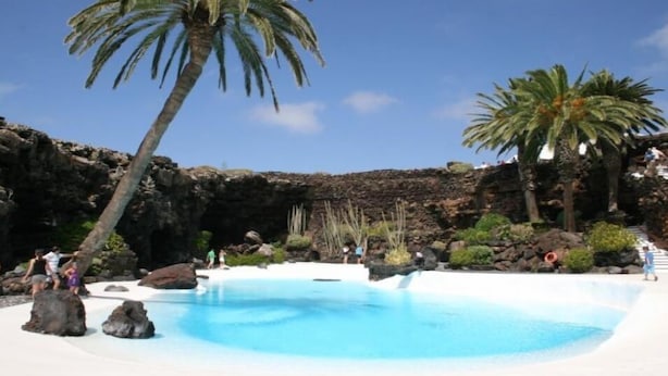 Un área de piscina con un paisaje rocoso, palmeras y un cielo azul despejado.