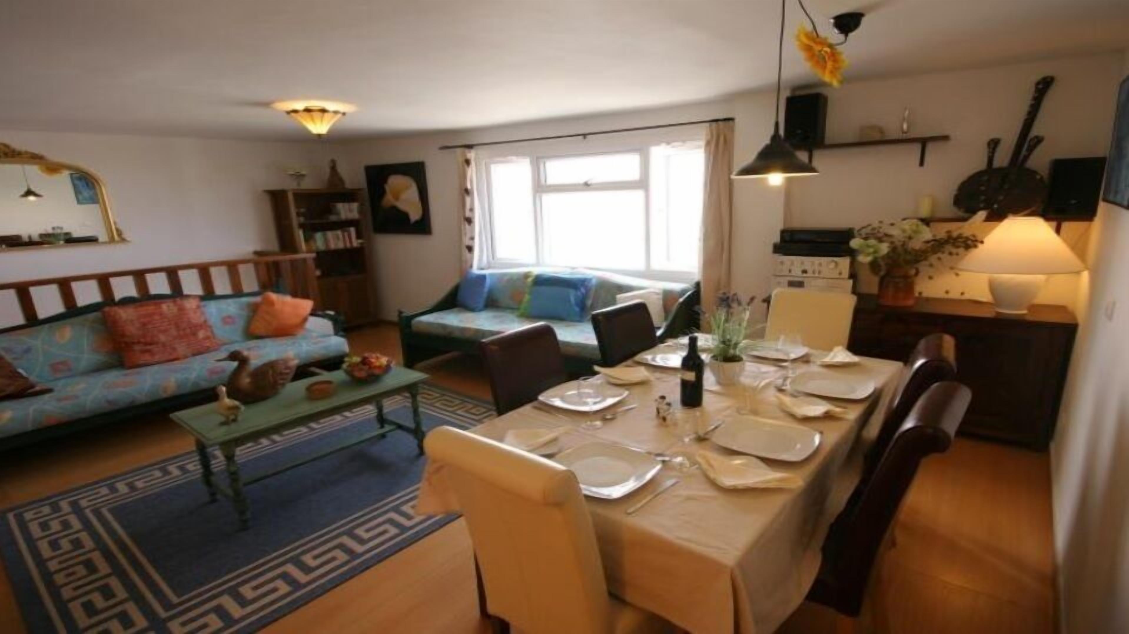 A cozy living room with a sofa, a dining table set for two, and a kitchen area with a stove and cabinets.