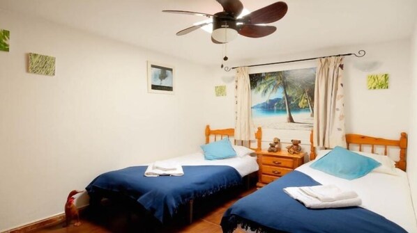 A bedroom with two single beds, a ceiling fan, a nightstand, and a beach-themed painting on the wall. - Luxury Apartment with Pool, Hot Tub, and Free Accommodation Insurance, (Teguise)