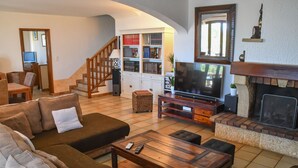 Ein Wohnzimmer mit Sofa, Couchtisch, Fernseher, Kamin, Bücherregal und einer Treppe.