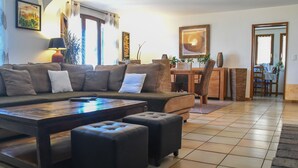 Ein Wohnzimmer mit einer Couch, Poufs, einem Couchtisch und einem Essbereich mit Stühlen und einem Tisch.