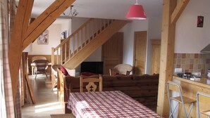 A cozy room with a wooden staircase, a dining table with a checkered tablecloth, and a kitchen area with a red hanging light. - Large 5-room duplex in town center, sleeps 10, near cable car, superb views (Saint-Gervais-Les-Bains)