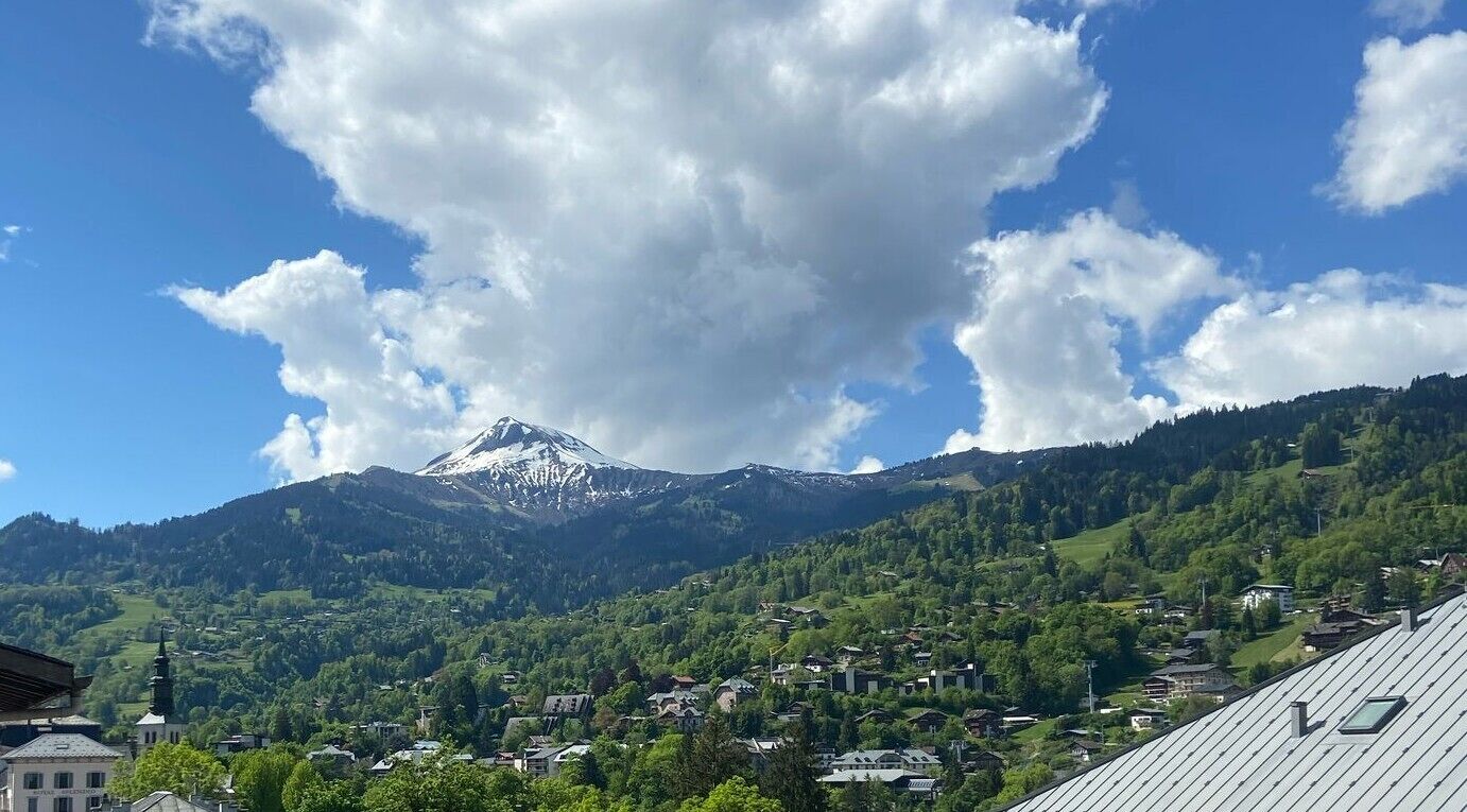 Une montagne dont le sommet est coiffé de neige, un village avec des maisons et une église surmontée d’une flèche.