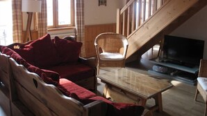 A cozy living room with a wooden staircase, a sofa, a chair, a coffee table, and a TV. - Large 5-room duplex in town center, sleeps 10, near cable car, superb views (Saint-Gervais-Les-Bains)