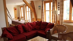 A cozy living room with a red sofa, wicker chairs, a wooden coffee table, and large windows with curtains. - Large 5-room duplex in town center, sleeps 10, near cable car, superb views (Saint-Gervais-Les-Bains)