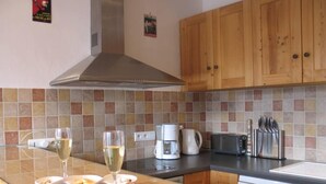 A kitchen with wooden cabinets, a tiled backsplash, a stainless steel range hood, a coffee maker, a toaster, and a cutting board with a knife and a piece of meat. - Large 5-room duplex in town center, sleeps 10, near cable car, superb views (Saint-Gervais-Les-Bains)