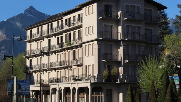 A multi-story hotel with balconies, a mountain view, and a sign indicating a restaurant on the ground floor. - Large 5-room duplex in town center, sleeps 10, near cable car, superb views (Saint-Gervais-Les-Bains)
