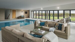 A modern indoor swimming pool area with wicker furniture and large windows. - Swallow's Orchard - Glastonbury (Glastonbury)