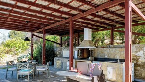 An outdoor patio with a stone wall, a grill, wicker furniture, and a stone table.