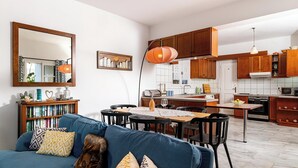 A modern living room with a blue sofa, a dining area with a table and chairs, and a kitchen with wooden cabinets and appliances.