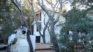 Una casa rústica con un muro de piedra, un comedero de pájaros de madera y una escalera de baldosas que conduce a un balcón.