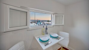 En spiseplads med udsigt over lystbådehavnen, et bord dækket med tallerkener, glas og bestik, samt en flaske vin.