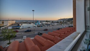 Udsigt fra en balkon over en lysthavn med både, parkeringsplads og en strand.