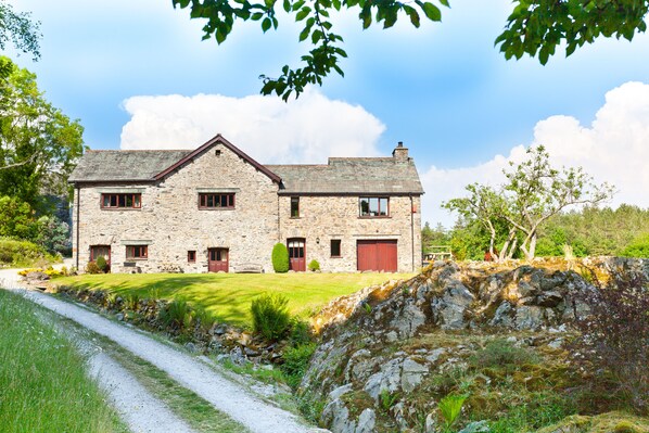 Une maison en pierre avec un toit en pente, deux cheminées et une porte rouge.