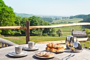 Une table en bois, mise avec une tasse, une soucoupe, des croissants, une assiette de pâtisseries, une théière et des couverts.