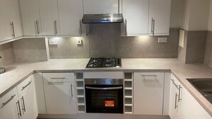 Cuina moderna amb armaris blancs, forn encastrat, fogó a gas i campana extractora d'acer inoxidable.
