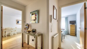Passadís amb terra de fusta, una taula amb un telèfon i un bol, un mirall amb notes, un radiador i una televisió a una habitació.