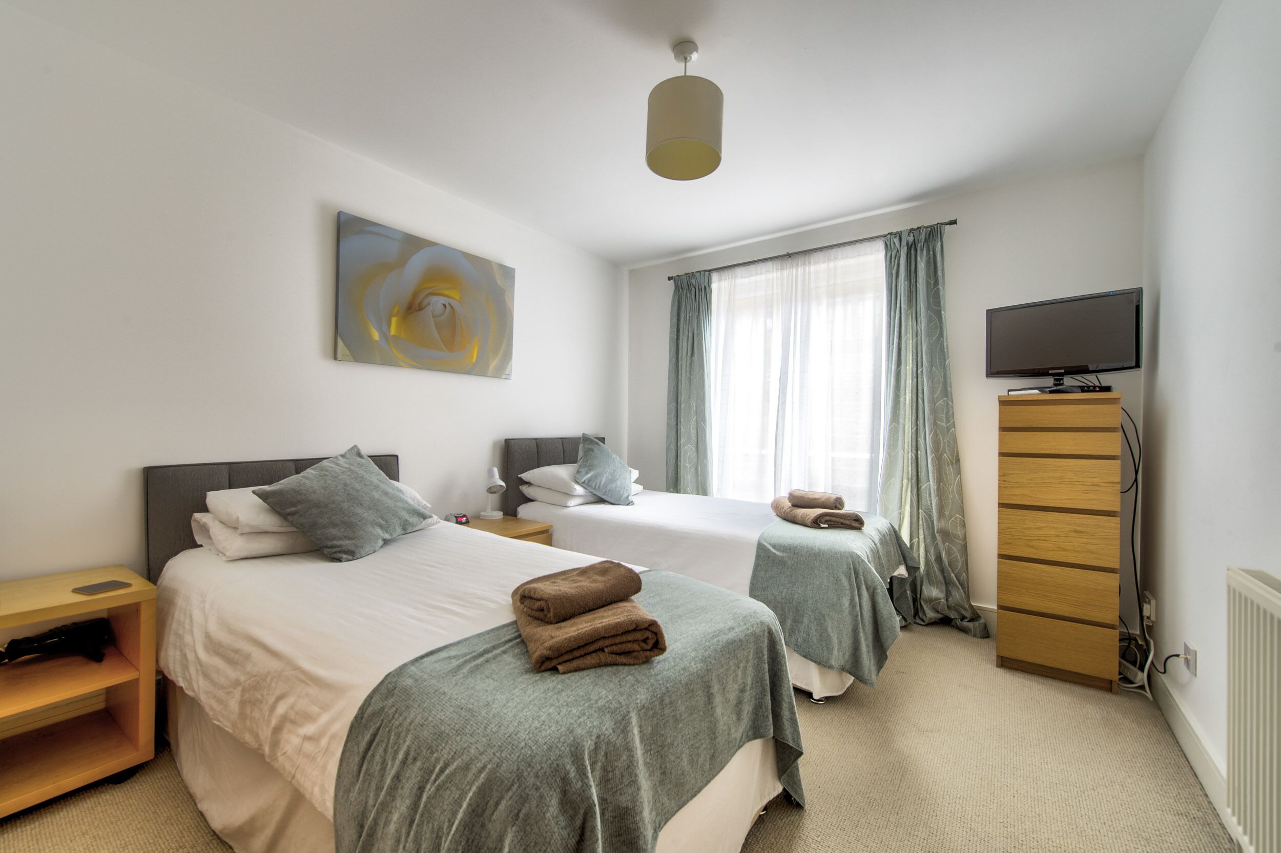 A hotel room with two beds, a TV, a dresser, and a painting on the wall.