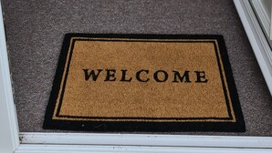 Een gang die leidt naar een deur met een 'WELCOME' mat.