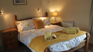 Een netjes opgemaakt bed met bloemenbedrukking, een bedlampje en een ingelijste citaat aan de muur.