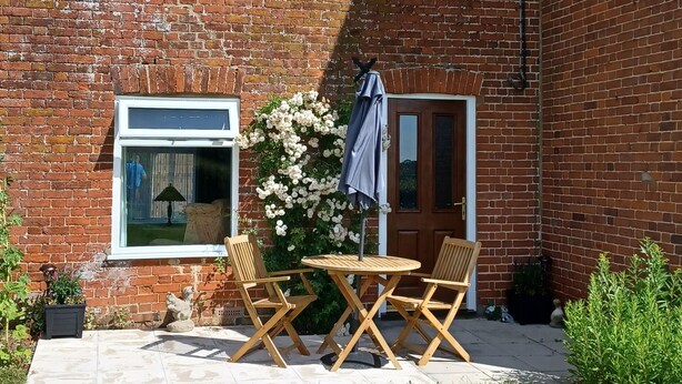 Een stenen huis met een terras, een tafel en stoelen, en een raam.