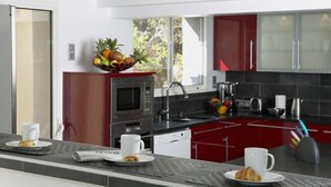A modern kitchen with red cabinets, a microwave, and a fruit bowl on the counter. - Superb villa "feet in the water"  (Roquebrune-Sur-Argens)