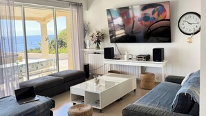 A modern living room with a large TV, comfortable seating, a coffee table, and a view of the sea. - Superb villa "feet in the water"  (Roquebrune-Sur-Argens)