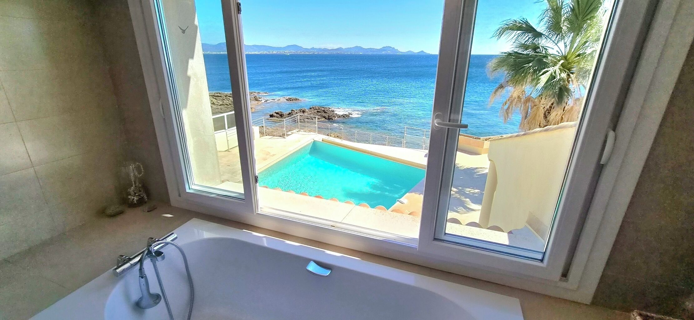 A bathroom with a bathtub and a view of a pool and ocean.